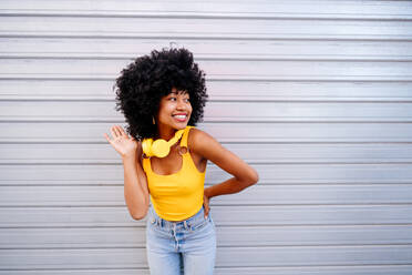 Schöne junge glückliche afrikanische Frau mit Afro-Lockenfrisur schlendert in der Stadt - Fröhliche schwarze Studentin Porträt auf bunten Wand Hintergrund - DMDF05983