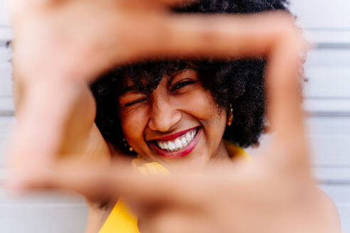 Schöne junge glückliche afrikanische Frau mit Afro-Lockenfrisur schlendert in der Stadt - Fröhliche schwarze Studentin Porträt auf bunten Wand Hintergrund - DMDF05984
