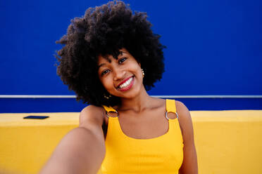 Beautiful young happy african woman with afro curly hairstyle strolling in the city - Cheerful black student portrait on colorful wall background - DMDF05995