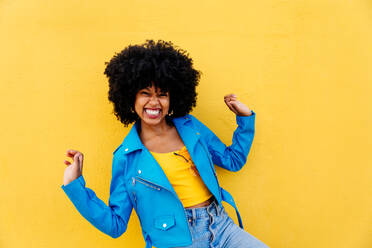 Junge afrikanische Frau mit Afro-Lockenfrisur genießt Stadtbummel - fröhliches Porträt einer schwarzen Studentin vor buntem Wandhintergrund - DMDF06018