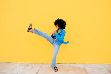 Beautiful young happy african woman with afro curly hairstyle strolling in the city - Cheerful black student portrait on colorful wall background - DMDF06019