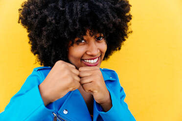 Beautiful young happy african woman with afro curly hairstyle strolling in the city - Cheerful black student portrait on colorful wall background - DMDF06020