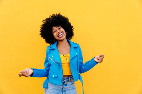 Beautiful young happy african woman with afro curly hairstyle strolling in the city - Cheerful black student portrait on colorful wall background - DMDF06022