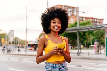 Junge afrikanische Frau mit Afro-Lockenfrisur genießt einen Spaziergang durch die Stadt - glückliches Studentenmädchen in Bewegung - DMDF06036