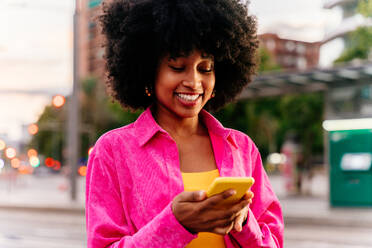 Beautiful young happy african woman with afro curly hairstyle strolling in the city - Cheerful black student girl walking on the street in the evening - DMDF06040