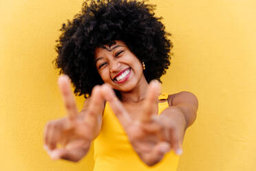 Junge, glückliche afrikanische Frau mit Afro-Lockenfrisur genießt einen Spaziergang in der Stadt - Porträt einer fröhlichen schwarzen Studentin vor einer bunten Wand - DMDF06244