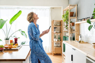 Reife Frau genießt ihr Zuhause und entspannt sich in ihrer Freizeit - 50-60 Jahre alt, elegant und mit Smartphone online - DMDF06247