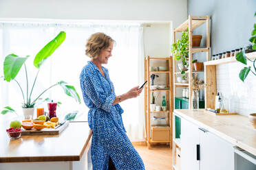 Reife Frau genießt ihr Zuhause und entspannt sich in ihrer Freizeit - 50-60 Jahre alt, mit Smartphone im Internet surfen - DMDF06248