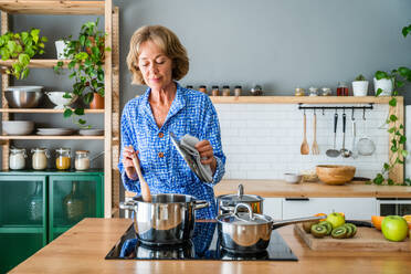 Reife Frau genießt häusliches Leben und Freizeitmomente - 50-60 Jahre alt, während sie Mittagessen in der Küche kocht - DMDF06260
