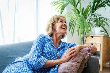 Eine schöne ältere Frau genießt ihr häusliches Leben und entspannt auf dem Sofa - im Alter von 50-60 Jahren - DMDF06307