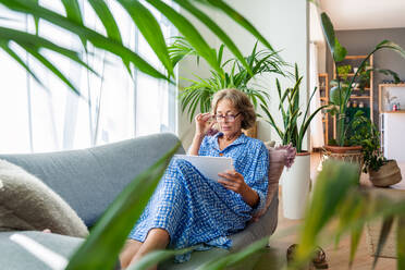 Entspannte ältere Frau genießt ihr Zuhause und Freizeit - eine hübsche 50-60-jährige weibliche Erwachsene auf dem Sofa - DMDF06311
