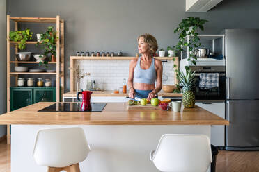 Sportliche ältere Frau genießt gesunde Mahlzeit nach dem Training zu Hause - 50-60 Jahre alt, aktiv und fit im Alltag - DMDF06407