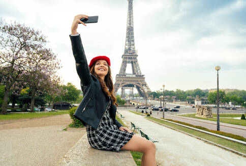 Junge Frau mit rotem Hut und modischer Kleidung erkundet Paris und den Eiffelturm, während sie sich im Stadtzentrum und bei Sehenswürdigkeiten vergnügt - DMDF06429