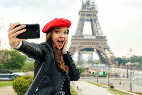 Junge Frau mit rotem Hut und modischer Kleidung besucht Paris und den Eiffelturm und genießt das Stadtzentrum und die Sehenswürdigkeiten - DMDF06430