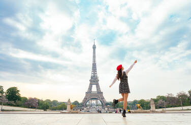 Eine junge Frau mit rotem Hut und modischer Kleidung besucht Paris und den Eiffelturm und genießt die Sehenswürdigkeiten der Stadt - DMDF06432