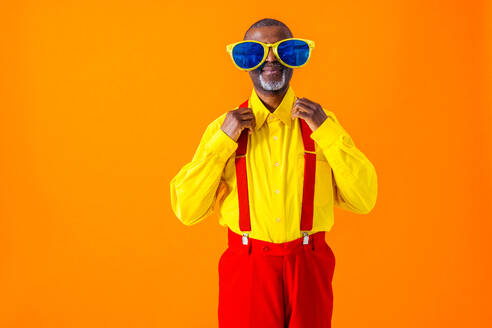 Stilvoller Rentner mit exzentrischer Kleidung und humorvollem Charakter posiert auf farbigem Hintergrund - DMDF06456