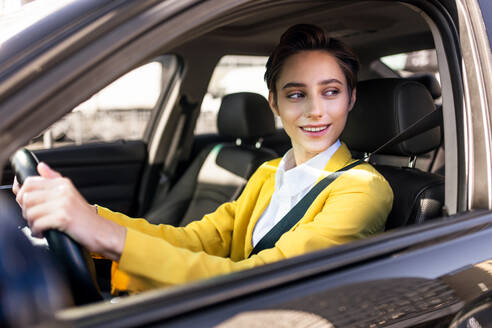 Beautiful young woman with short hair driving car in the city - Pretty caucasian female adult business woman wearing elegant suit going to work in the office - DMDF06458