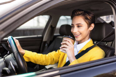 Beautiful young woman with short hair driving car in the city - Pretty caucasian female adult business woman wearing elegant suit going to work in the office - DMDF06467