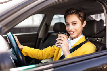 Beautiful young woman with short hair driving car in the city - Pretty caucasian female adult business woman wearing elegant suit going to work in the office - DMDF06468