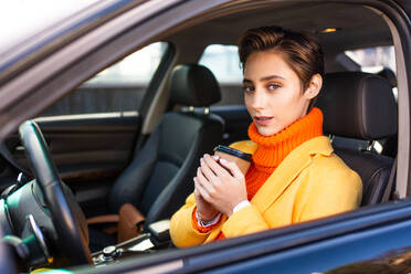 Beautiful young woman with short hair driving car in the city - Pretty caucasian female adult business woman wearing elegant suit going to work in the office - DMDF06472