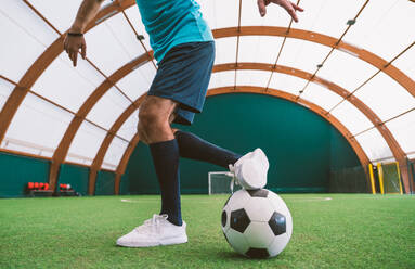 Cinematic image of a soccer freestyle player making tricks with the ball on a artificial grass court indoor. Concept about sport and people lifestyle - DMDF06518