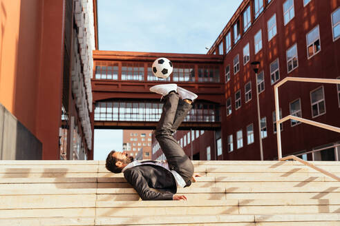Bild eines Geschäftsmannes und eines Fußball-Freestyle-Spielers, der auf der Straße Tricks mit dem Ball macht. Konzept über Sport und Geschäftsleute - DMDF06537