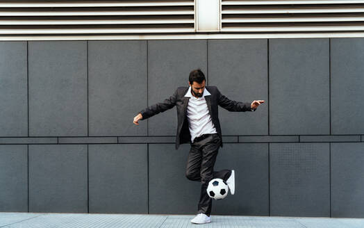 Bild eines Geschäftsmannes und eines Fußball-Freestyle-Spielers, der auf der Straße Tricks mit dem Ball macht. Konzept über Sport und Geschäftsleute - DMDF06541