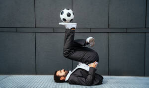 Bild eines Geschäftsmannes und eines Fußball-Freestyle-Spielers, der auf der Straße Tricks mit dem Ball macht. Konzept über Sport und Geschäftsleute - DMDF06542