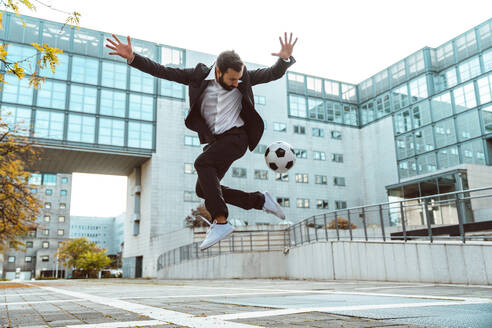 Bild eines Geschäftsmannes und eines Fußball-Freestyle-Spielers, der auf der Straße Tricks mit dem Ball macht. Konzept über Sport und Geschäftsleute - DMDF06543