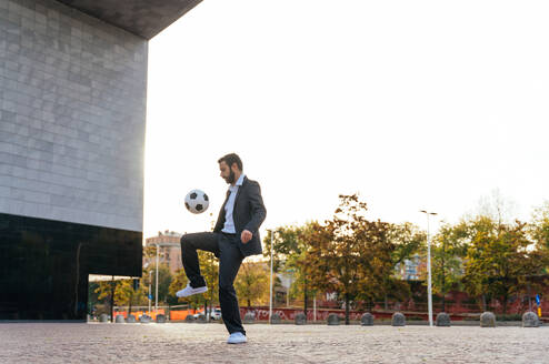 Bild eines Geschäftsmannes und eines Fußball-Freestyle-Spielers, der auf der Straße Tricks mit dem Ball macht. Konzept über Sport und Geschäftsleute - DMDF06548