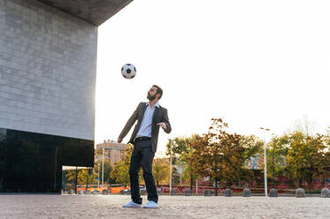 Bild eines Geschäftsmannes und eines Fußball-Freestyle-Spielers, der auf der Straße Tricks mit dem Ball macht. Konzept über Sport und Geschäftsleute - DMDF06549