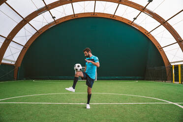 Cinematic Bild eines Fußball-Freestyle-Spieler macht Tricks mit dem Ball auf einem Kunstrasenplatz Indoor. Konzept über Sport und Menschen Lebensstil - DMDF06552