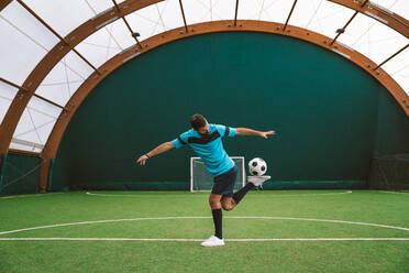 Cinematic Bild eines Fußball-Freestyle-Spieler macht Tricks mit dem Ball auf einem Kunstrasenplatz Indoor. Konzept über Sport und Menschen Lebensstil - DMDF06553