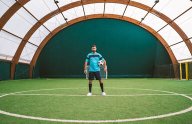 Cinematic Bild eines Fußball-Freestyle-Spieler macht Tricks mit dem Ball auf einem Kunstrasenplatz Indoor. Konzept über Sport und Menschen Lebensstil - DMDF06554