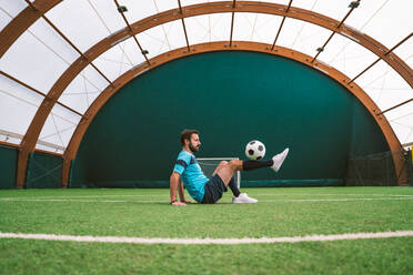 Cinematic Bild eines Fußball-Freestyle-Spieler macht Tricks mit dem Ball auf einem Kunstrasenplatz Indoor. Konzept über Sport und Menschen Lebensstil - DMDF06555