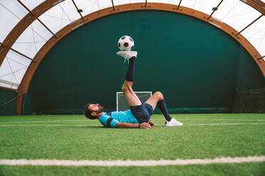 Cinematic Bild eines Fußball-Freestyle-Spieler macht Tricks mit dem Ball auf einem Kunstrasenplatz Indoor. Konzept über Sport und Menschen Lebensstil - DMDF06556
