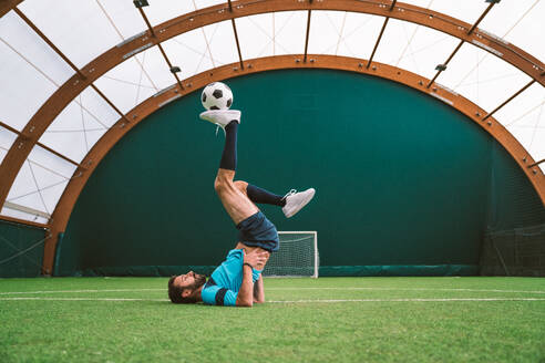 Cinematic image of a soccer freestyle player making tricks with the ball on a artificial grass court indoor. Concept about sport and people lifestyle - DMDF06557