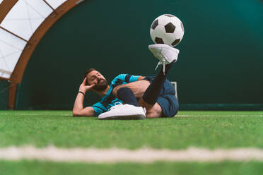 Cinematic Bild eines Fußball-Freestyle-Spieler macht Tricks mit dem Ball auf einem Kunstrasenplatz Indoor. Konzept über Sport und Menschen Lebensstil - DMDF06558