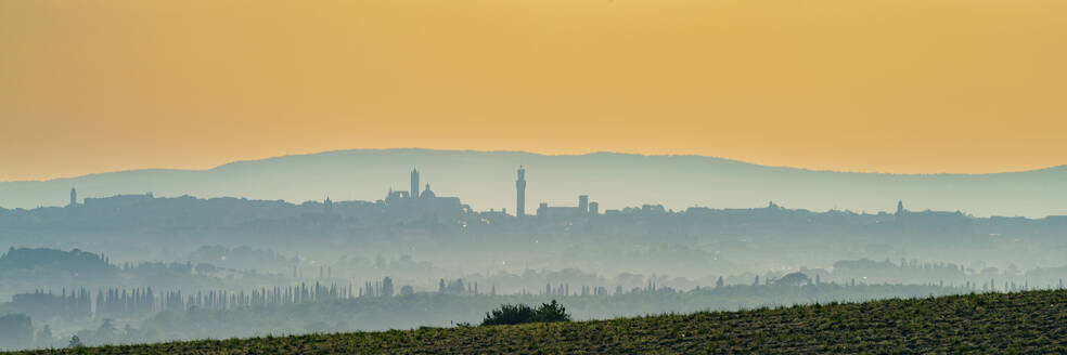 Italy, Tuscany, Siena, Panoramic view of hills and distant city at foggy dawn - WGF01497