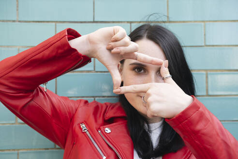 Young woman looking through finger frame in front of wall - AMWF01704