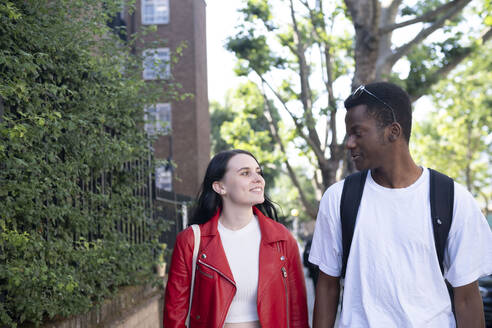 Happy man and woman walking together in front of tree - AMWF01719