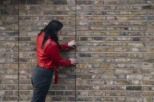 Young woman opening door near brick wall - AMWF01748