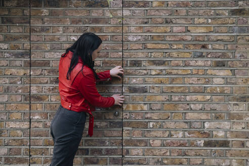 Young woman opening door near brick wall - AMWF01748