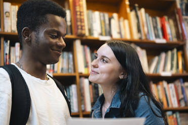 Lächelnder Mann und lächelnde Frau schauen sich in der Bibliothek an - AMWF01765