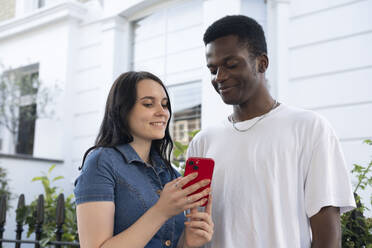Lächelnder Mann mit Frau, die ein Smartphone vor einem Gebäude benutzt - AMWF01773