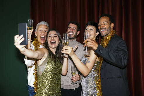 Family with champagne glasses taking selfie on mobile phone in new year party at home - EBSF03832