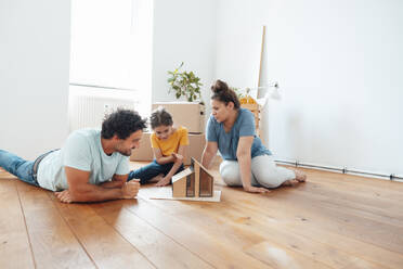 Happy family looking at model house on floor - JOSEF21148