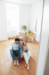 Happy man and woman sitting on floor at home - JOSEF21155