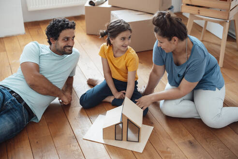 Happy family sitting with model house on floor at home - JOSEF21166