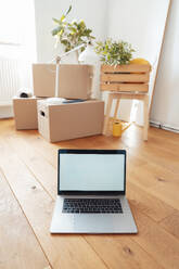 Laptop with cardboard boxes on floor at home - JOSEF21203